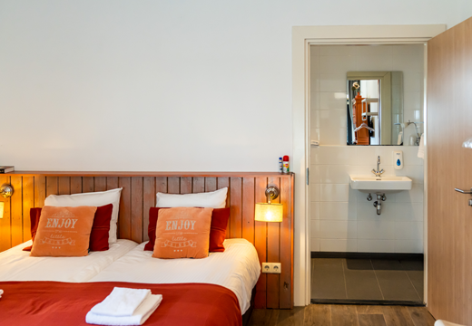 kamer betje, tweepersoons kamer hotelkamer op de johanneshoeve, tweepersoonsbed met daarop oranje kussentjes en rode sprei, badkamer ensuite